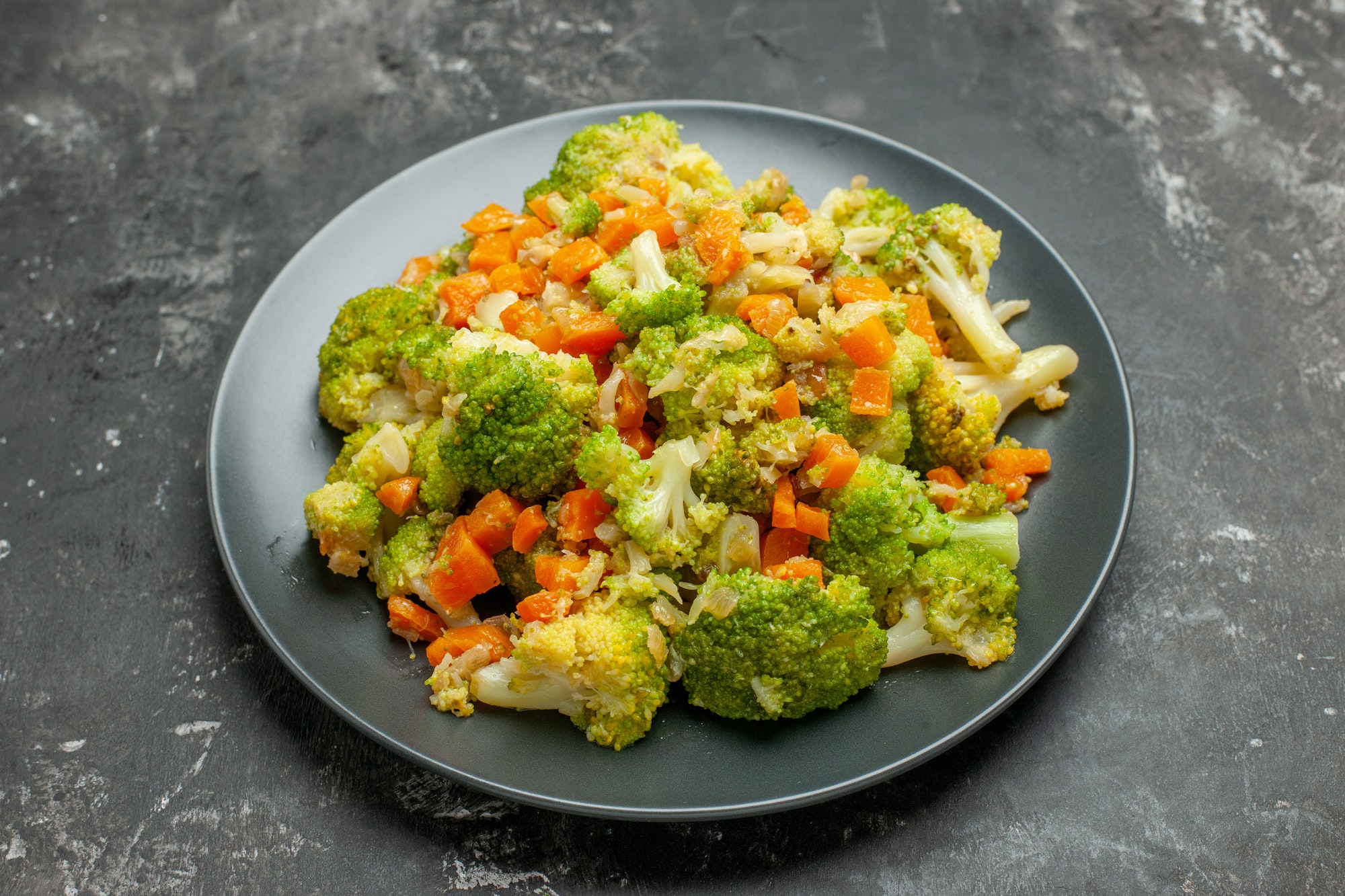 Half shot of healthy meal with brocoli and carrots on a black plate on gray background